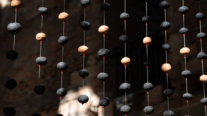 Strings of black and earth coloured clay beads are suspended on strings. The background is dark.